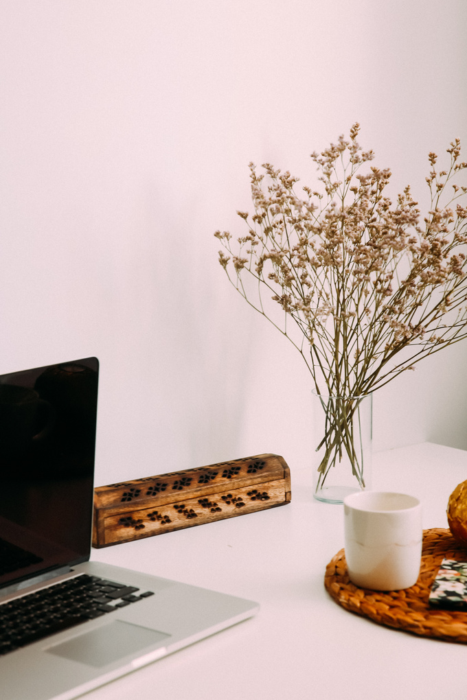 Home office workspace with laptop, candle holder, mug, notebook, grass bouquet. Light aesthetic hygge space. Freelance work, business workplace.